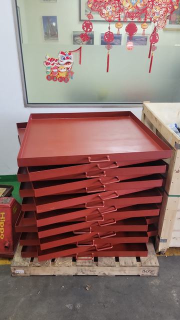 Stack of red-painted steel trays with handles